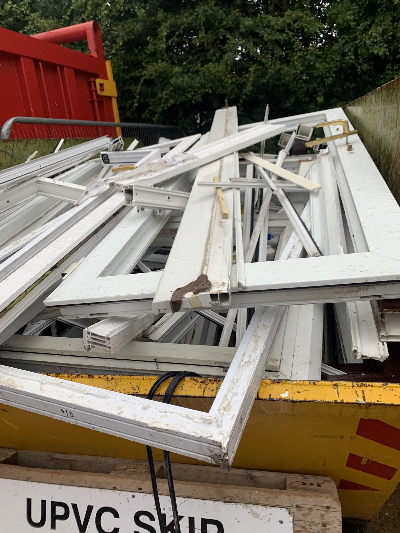 Stack of post-consumer uPVC window frames loaded into a UPVC SKIP at a UK trade recycling depot